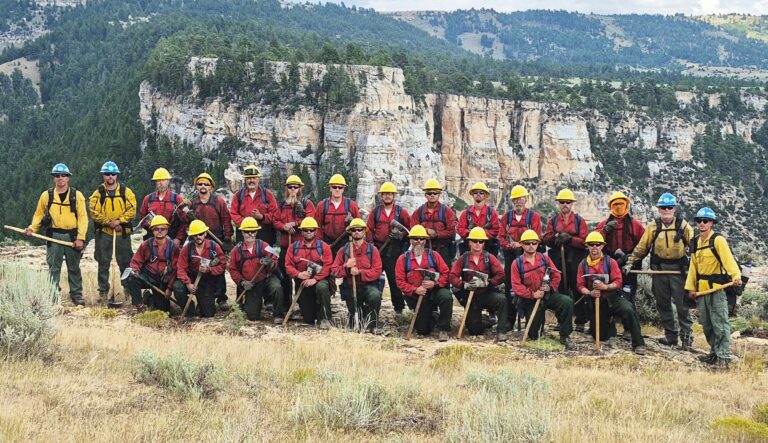 A group of men in yellow and red shirts post in front of a Wyoming landscape