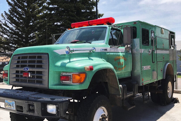 A green fire-fighting vehicle from the Vedauwoo Volunteer Fire Department is parked in a cement lot.
