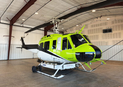Side view of a lime-green helicopter, sitting inside a helibase.